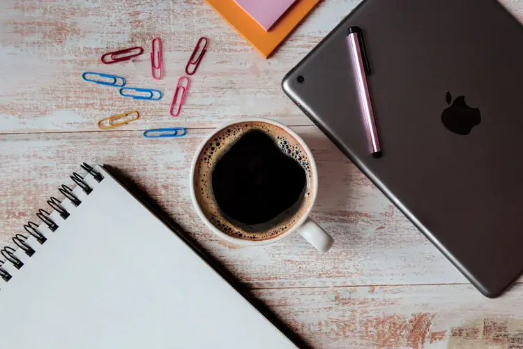 Tablet, notebook, and coffee on a desk, representing straightforward business planning.